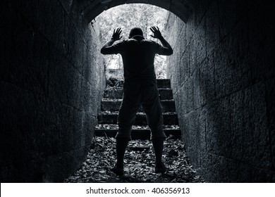 Man Leaves Dark Stone Tunnel With Raised Hands, Surrender Concept Black And White Photo 