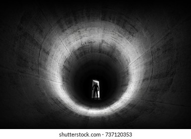 A man leaves opening door from dark concrete tunnel and looks outside to the light