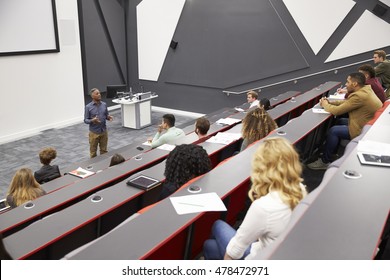 Man lectures students in lecture theatre, mid row seat POV