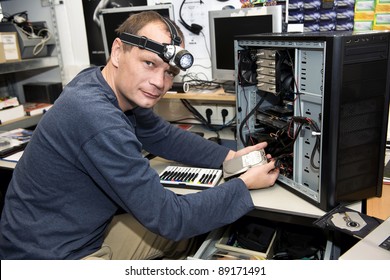 Man With A LED Light On His Head, Working On A Desk Top Computer In A Computer Repair Shop