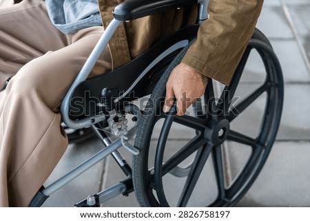 A man with a leg disability who cannot walk uses a wheelchair and travels by the train at a station He walks along the sidewalk where there are signs indicating accessibility for disabled individuals