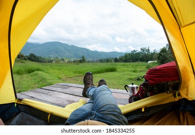 Man legs in blue jeans and hiking shoe lying down in yellow tent with backpack on mountain. Loneliness man tourist backpacker relax and enjoy beautiful nature outdoor lifestyle and holiday vacation.