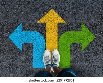  man legs in sneakers standing on road with three direction arrow choices, left, right or move forward  - Shutterstock ID 2204992851