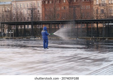 Man Leveling With Water Ice Rink For Outdoor Hockey Game Or Public Skating Area For Winter Season. Worker Filling City Square For Skate Rink In Wintertime. Leisure Activities During Christmas Holidays