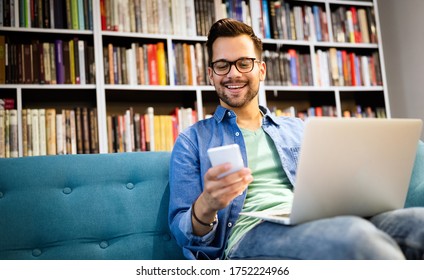 Man In Library Talking On Cell Phone And Working On Laptop