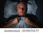 Man lies awake in bed at night with an anxious face