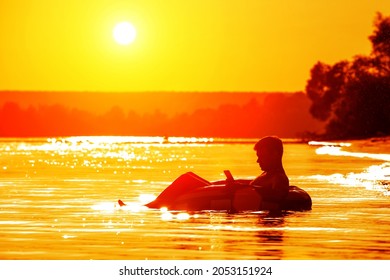 A man lies on an inflatable ring holding a phone in his hands at sunset. Relax after a day at work. The traveler enjoys nature, warm weather and beautiful sunsets.