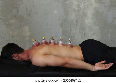 A man lies on a massage table with massage cans on an grey concrete background. Cupping massage concept. 