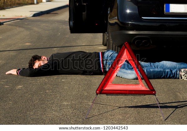 The man lies\
on the road behind the black car and warning triangle.The car\
collided pedestrian was on the\
ground.