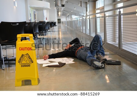 Man lies on the wet floor on which he slipped in spite of caution sign, selective focus on man's head