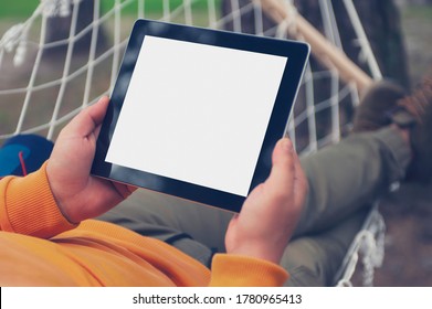 Man lies and rests in a hammock with a mock-up of a tablet with a white screen in his hands - Powered by Shutterstock