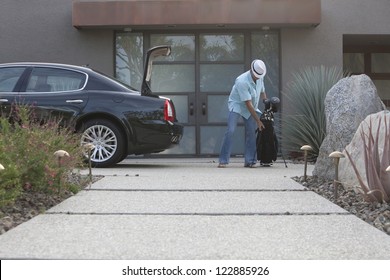 Man Lifting Golf Bag Into Boot Of Car