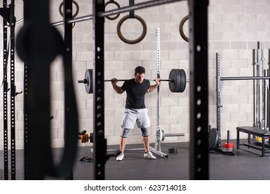 Man Lifting Heavy Barbell On Squat Rack, Gym Equipment In Foreground