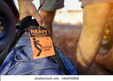 Man Lifting Heavy Duty Luggage Bag With Hand And Have Caution Tag Sign Attached  