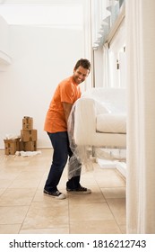 Man Lifting White Sofa Wrapped In Plastic Sheet Through Doorway In Sparse Room While Moving House.