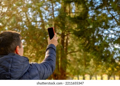 Man Lifts A Cell Phone In Nature. Concept Of Wifi Connection, Internet Line Coverage.