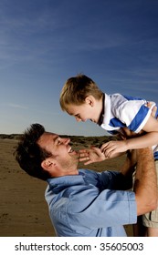 A man lifts his son into the air at the beach