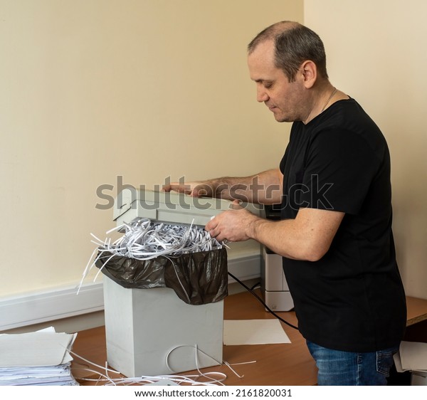 the man lifts the upper cutting part of the\
shredder. shredder basket filled with cut paper. destruction of\
confidential information