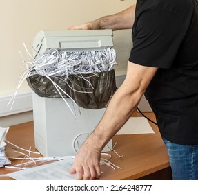 the man lifts the upper part of the shredder. shredder basket filled with cut paper, destruction of confidential information