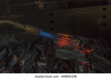 A Man IS Lighting Charcoal With Propane Torch On Home Made Grill Close Up