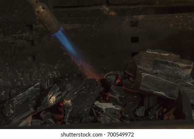 A Man IS Lighting Charcoal With Propane Torch On Home Made Grill Close Up