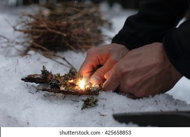 Man Lighting A Fire In A Dark Winter Forest, Preparing For An Overnight Sleep In Nature, Warming Himself With DIY Fire. Adventure, Scouting, Survival Concept. 
