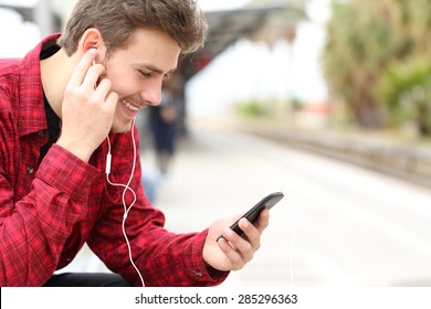 Man listening to the music with earbuds from a smart phone while is waiting in a train station 
