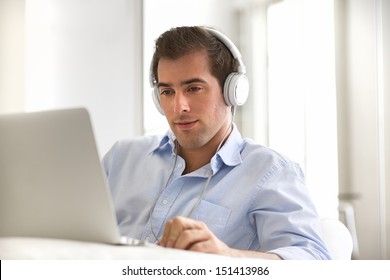 Man Listening To Music With Headphones On Laptop Computer, Sitting On Couch