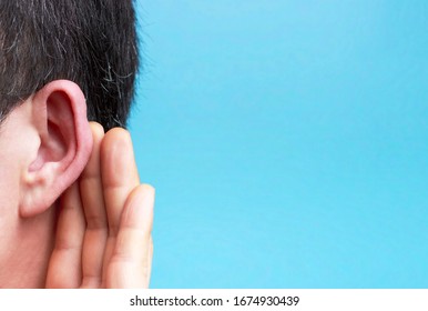 The man listens attentively with her palm to her ear close-up, a blue background