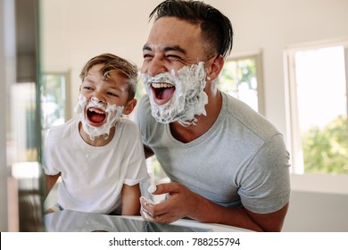 Man and little boy with shaving foam on their faces looking into the bathroom mirror and laughing. Father and son having fun while shaving in bathroom. - Shutterstock ID 788255794