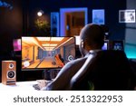 Man in living room playing video games on gaming PC at computer desk, enjoying day off from work. Gamer battling enemies in online multiplayer shooter from neon lights ornate home