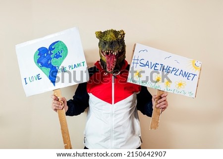 Man with a lizard head in studio WITH cardboard sign that says #SAVETHEPLANET and I LOVE THE PLANET