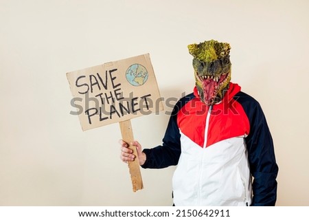 Man with a lizard head in studio WITH cardboard sign that says #SAVETHEPLANET