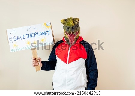 Man with a lizard head in studio WITH cardboard sign that says #SAVETHEPLANET