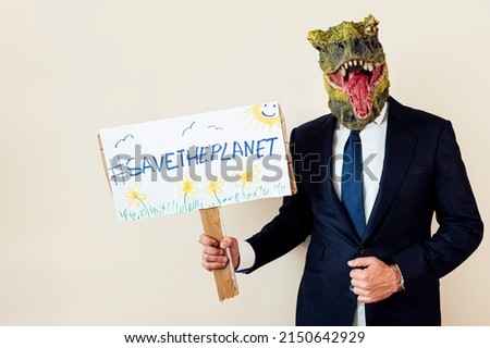 Man with a lizard head in studio WITH cardboard sign that says #SAVETHEPLANET