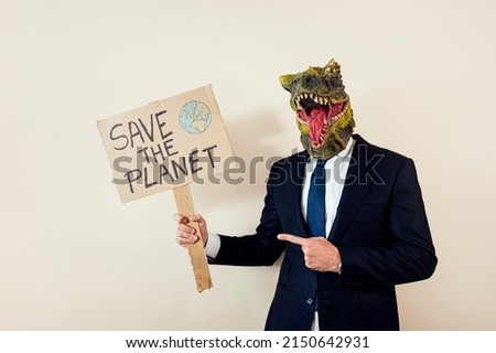 Man with a lizard head in studio WITH cardboard sign that says #SAVETHEPLANET