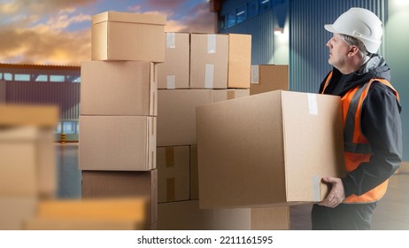 Man Loader. Human With Big Box In His Hands. Guy Works As Loader In Warehouse. Man With Boxes Next To Storage Sheds. Man Works In Warehouse Industry. Loader Worker In Orange Vest.