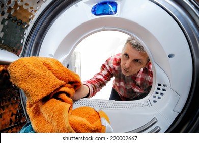 Man loading clothes to washing machine. View from the inside of washing machine.