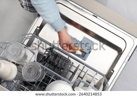 Man loading dishwasher with detergent tablet and dirty dishes in kitchen during daily cleaning routine
