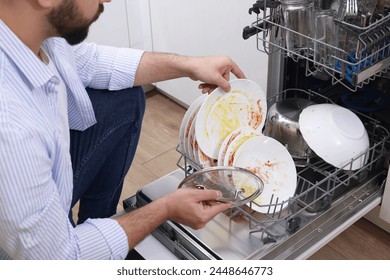 Man loading dishwasher with dirty plates indoors, closeup - Powered by Shutterstock