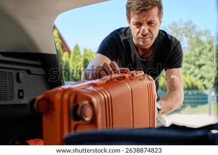 Man loading orange suitcase into open car trunk, inside view. Concept of travel preparation, packing for vacation or departure on road trip