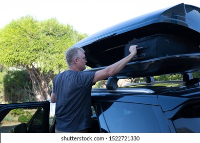 Man Loading Suitcase Into Roof Box On Top Of Car