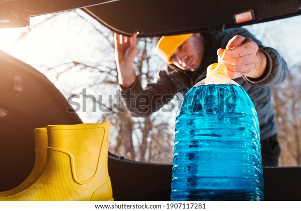 A man loads a backup\
canister of blue windshield washer fluid into the trunk of a car -\
antifreeze