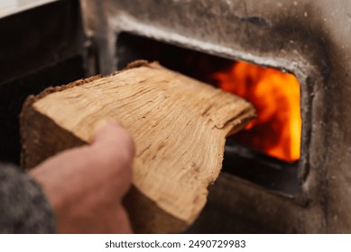 Man loads piece of firewood in the solid fuel boiler, flames on the background. Solid fuel and heating concept