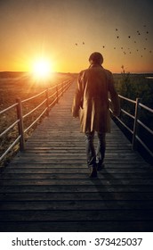 A Man With Long Coat Walking In A Boardwalk Into De Sunset