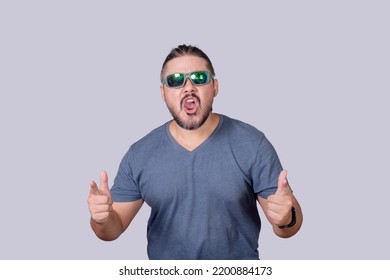 A man with long hair and wearing sunglasses acting tough and macho, pointing to the camera while yelling. Isolated on a gray background.