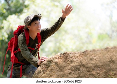 A Man In Long Sleev T-shirt, Long Camouflage Pants, Hiking Hat And Red Bagback Reach His Hand Up To The Sky Arsking For Help To Climb Up To The Slope Or Mountain. Adventure Activity Outdoor.