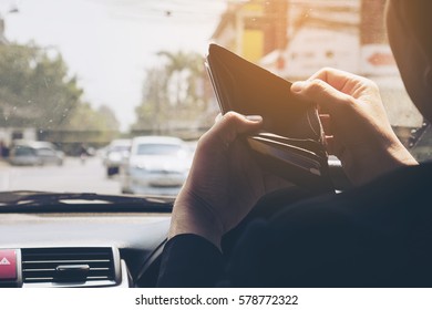 Man look at his empty wallet while driving car, dangerous behavior 