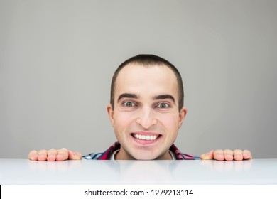 Man looking at camera, peeking from behind the desk, smiles, grey background, blank copy space, for your advertisement, for records or slogan, front view