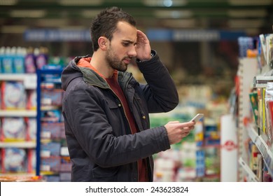 Man Looking Confused At Mobile Phone In Supermarket